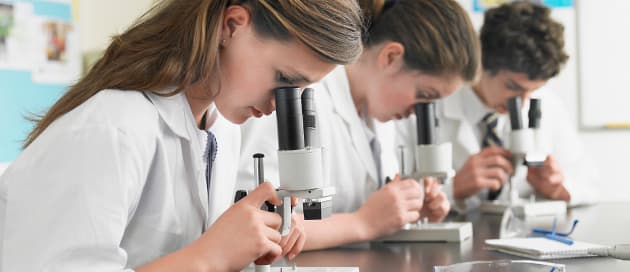 Three teenage students in lab coats look